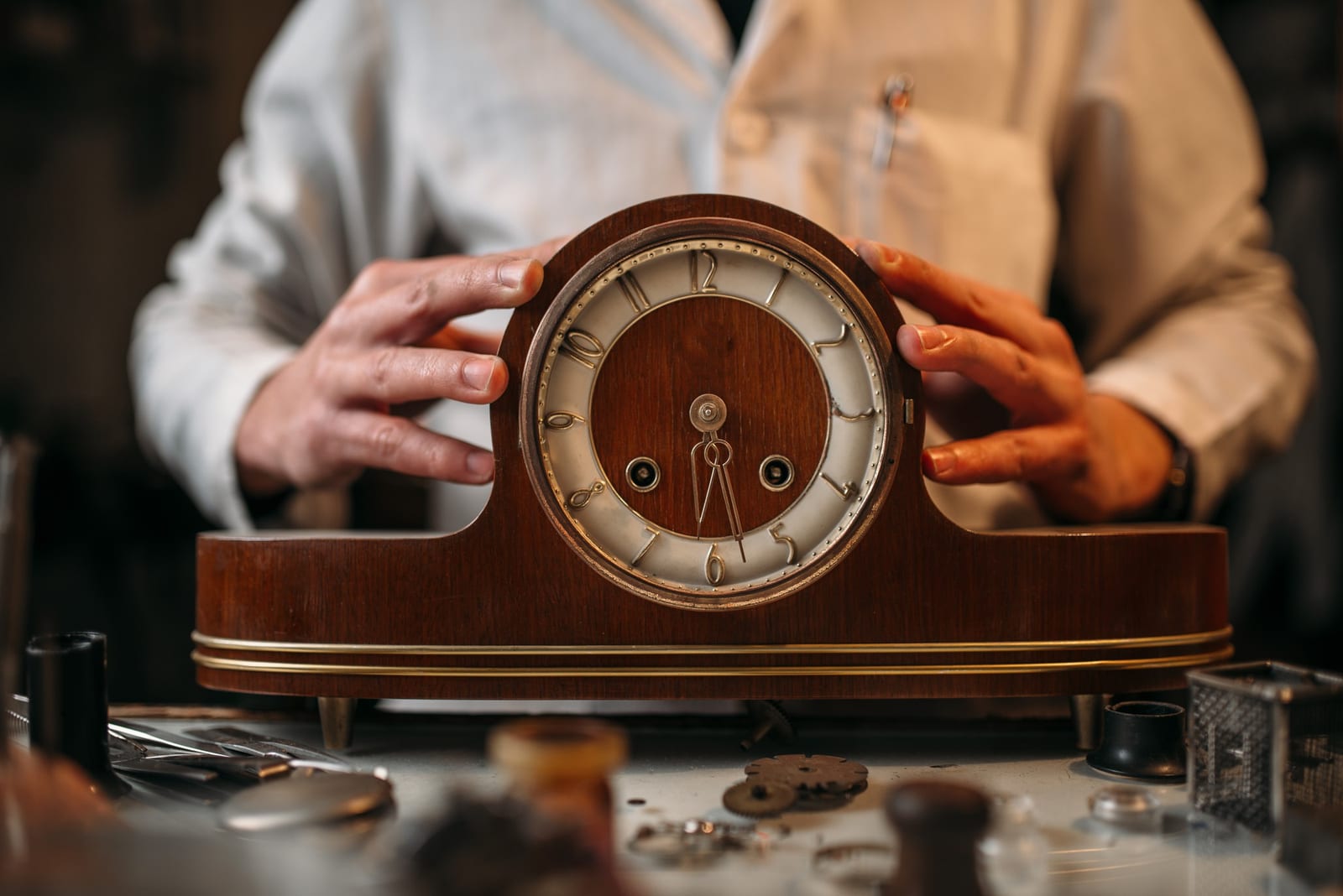 Un artigiano osserva il quadrante di un orologio da tavolo antico appena restaurato, tra gli strumenti del banco